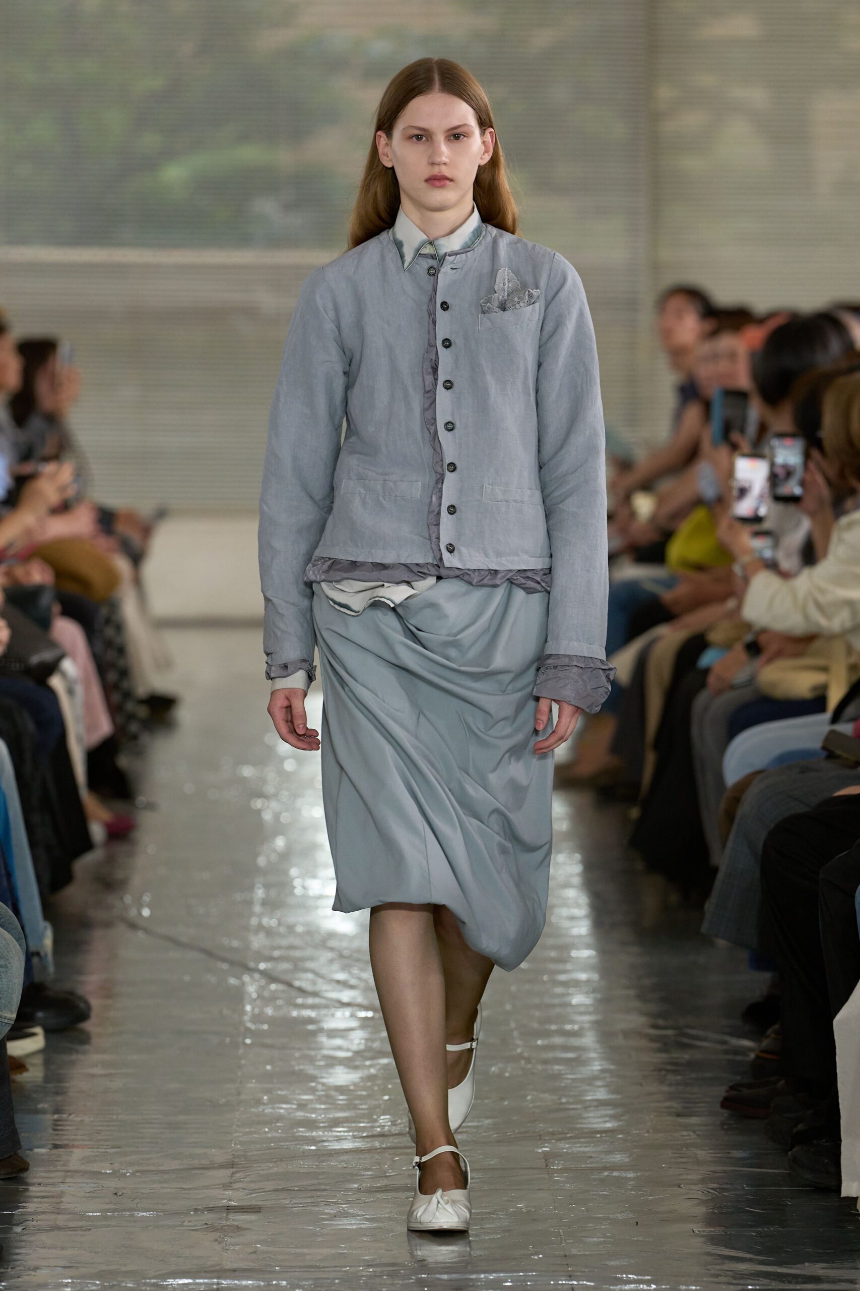 Powder-blue shirt jacket with puckered grey facing peeking at the placket and cuffs, over a pale pointed-collar shirt. Icy draped skirt twisted at the hip, white strap flats. Like crossing a quiet lobby before the florist opens.
